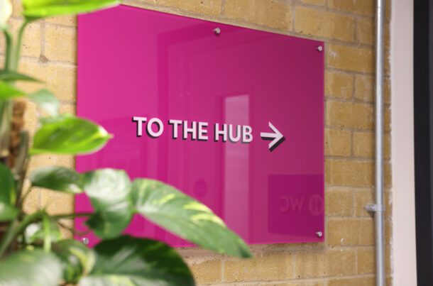 A purple sign on the wall of the Euston Community Hub directing people to the entrance